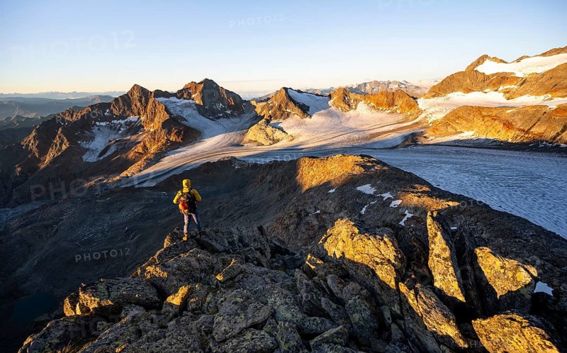 Mountaineers in front of a picturesque high mountain landscape at sunrise with alpenglow, glacier and rocky mountain peaks in the morning light, view at the Becher on mountain peak Königshofspitz and glacier Übeltalferner, Stubai Alps, South Tyrol, Italy, Europe
