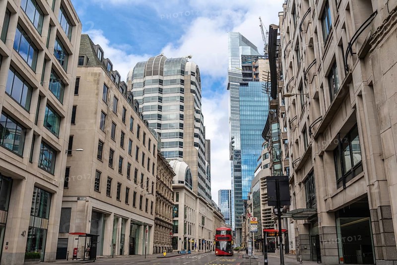 Red double decker bus driving on empty street surrounded by modern and historic buildings in city of london, united kingdom