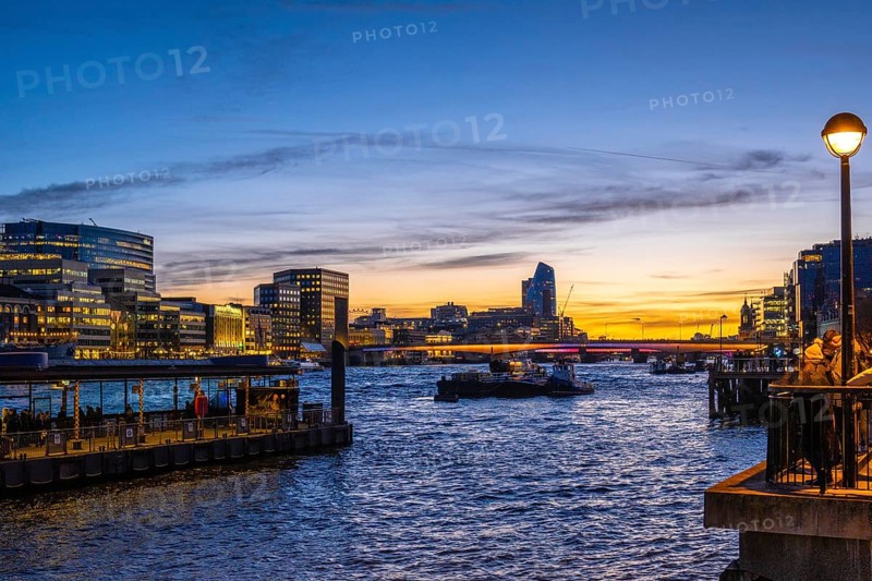 Tugboats sailing on thames during sunset with london's illuminated skyline reflecting on the water