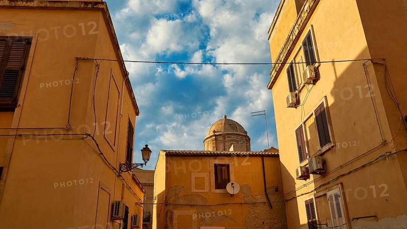 Narrowed view of a dome, framed by yellow houses and cables, with partly cloudy sky, Ortigia Island, Isola di Ortigia, Historic Centre, Syracuse, Sicily, Italy, Europe