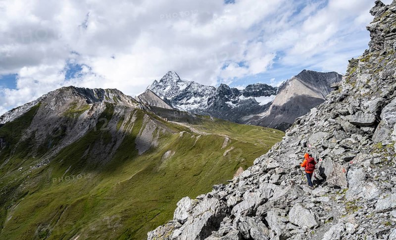 Mountaineer on steep rocky hiking trail, descent from the summit of Kastenegg, view of picturesque mountain landscape with snow-covered summit of the Großglockner, Wiener Höhenweg, Schober group, Hohe Tauern National Park, Carinthia, Austria, Europe