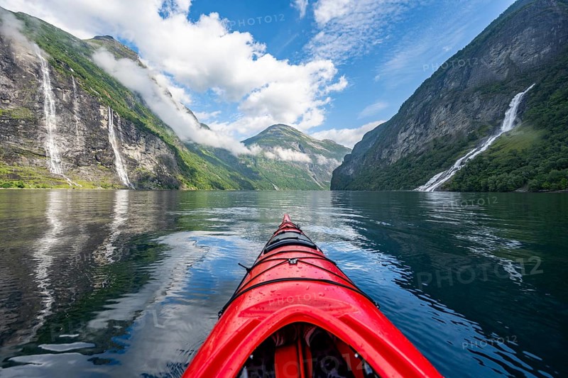 Kayak trip on the Geirangerfjord with waterfall The Seven Sisters and Freier Waterfall, tip of a red kayak in the fjord, atmospheric fjord landscape with reflection, first person view, near Geiranger, Møre og Romsdal, Norway, Europe