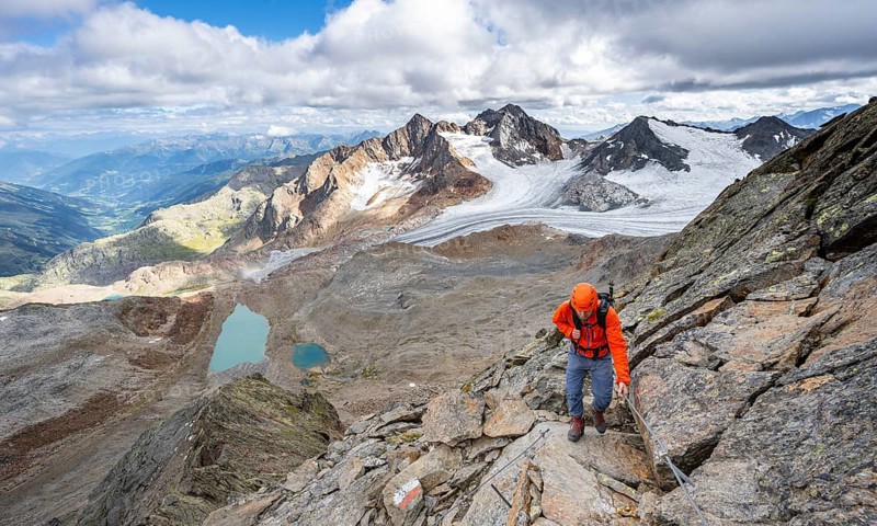 Mountaineer with helmet on a rope-insured path, in high mountain landscape, view of blue glacier lakes, mountain peaks Königshofspitz and Hofmannspitze with glacier of the Übeltalferner, Stubai Alps, South Tyrol, Italy, Europe