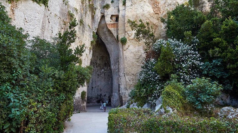 Cave Ear of Dionysus, Overgrown cave entrance with lush vegetation and rocks, people in the distance, Neapolis Archaeological Park, Syracuse, Sicily, Italy, Europe