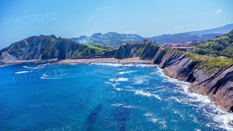 Breathtaking aerial view of zumaia's unique flysch coastline, showcasing its dramatic cliffs and inviting blue waters under a vibrant summer sky, Spain.