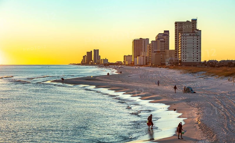 People walking and playing on the beach as the sun sets over the Gulf of Mexico at Gulf Shores, Alabama