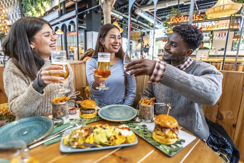 Happy multi ethnic friends toasting drinks and enjoying a delicious meal together at a lively restaurant, filled with laughter and joy