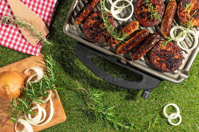 Barbecue with sausages and burgers, decorated with rosemary and onions on a green lawn