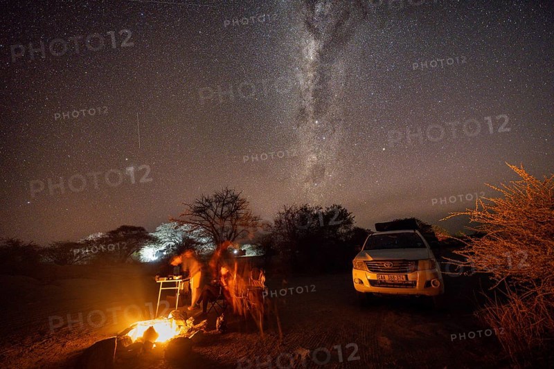 Tourists sitting around a campfire next to their off-road vehicle at night, night shot with starry sky and Milky Way, Kubu Island (Lekubu), Sowa Pan, Makgadikgadi Salt Pans, Botswana, Africa