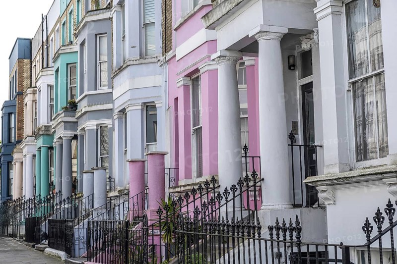 Pastel colored victorian terraced houses with ornate wrought iron fences create a picturesque street scene in london