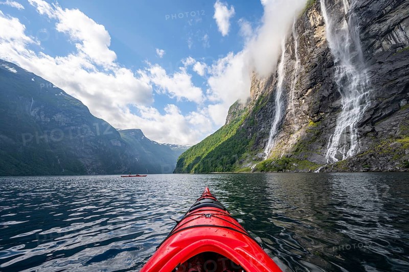Kayak trip on the Geirangerfjord at the waterfall The Seven Sisters, tip of a red kayak in the fjord, atmospheric fjord landscape, first person view, near Geiranger, Møre og Romsdal, Norway, Europe