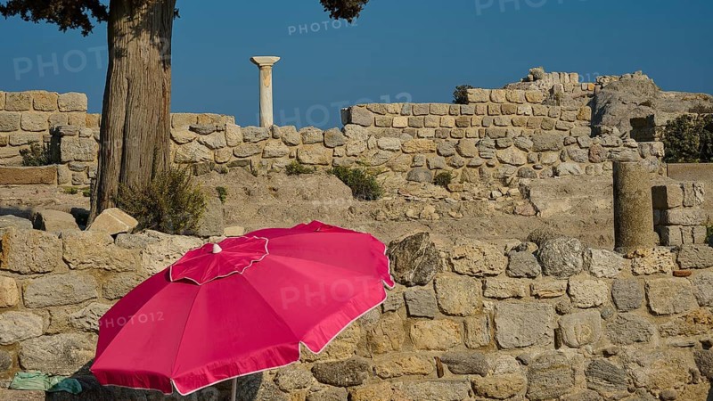 Ancient ruins with a red parasol in the foreground under a clear blue sky, Agios Stefanos Beach, Agios Stefanos Basilica, Chapel of Agios Nikolaos, Kastri Island, Kos, Dodecanese, Greek Islands, Greece, Europe