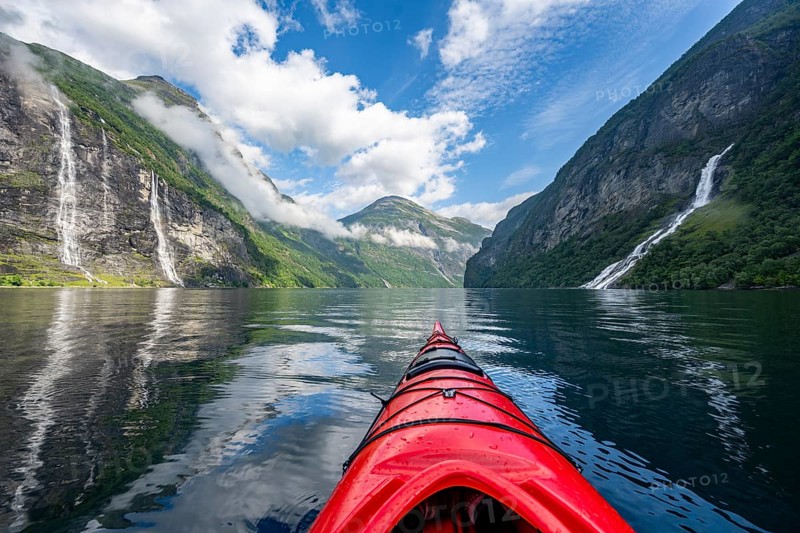 Kayak trip on the Geirangerfjord with waterfall The Seven Sisters and Freier Waterfall, tip of a red kayak in the fjord, atmospheric fjord landscape with reflection, first person view, near Geiranger, Møre og Romsdal, Norway, Europe