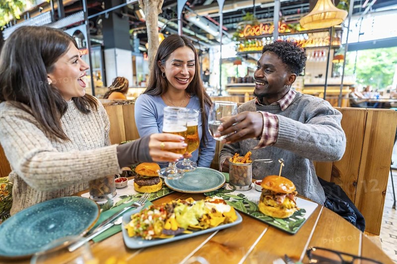 Young multi ethnic friends toasting with beer and water, enjoying a lively lunch filled with laughter and delicious food at a trendy restaurant
