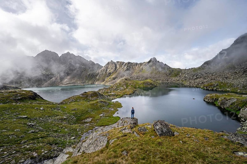 Mountaineer on a rock in front of mountain lakes Wangenitzsee and Kreuzsee, cloudy mountain peaks in the morning, Schober group, Hohe Tauern National Park, Carinthia, Austria, Europe