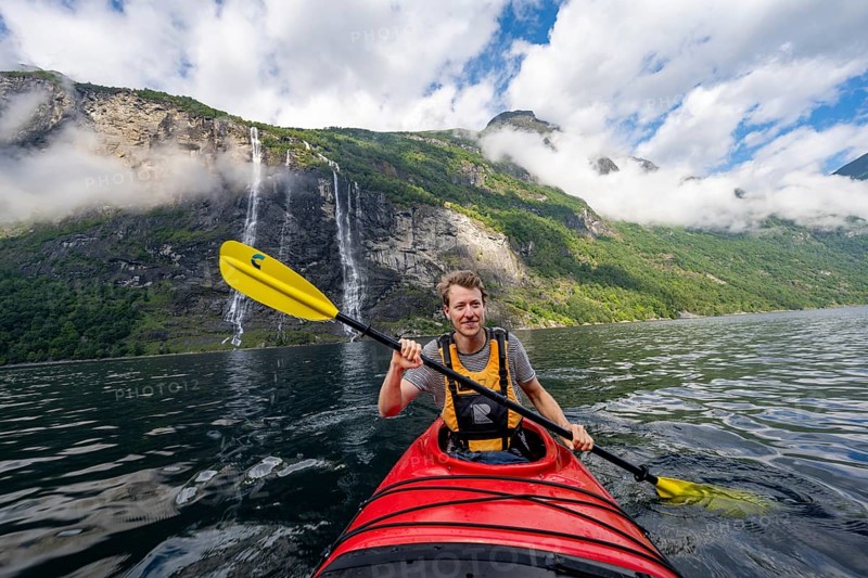 Kayak trip on the Geirangerfjord at the waterfall The Seven Sisters, Young man paddling in a kayak, atmospheric fjord landscape, near Geiranger, Møre og Romsdal, Norway, Europe