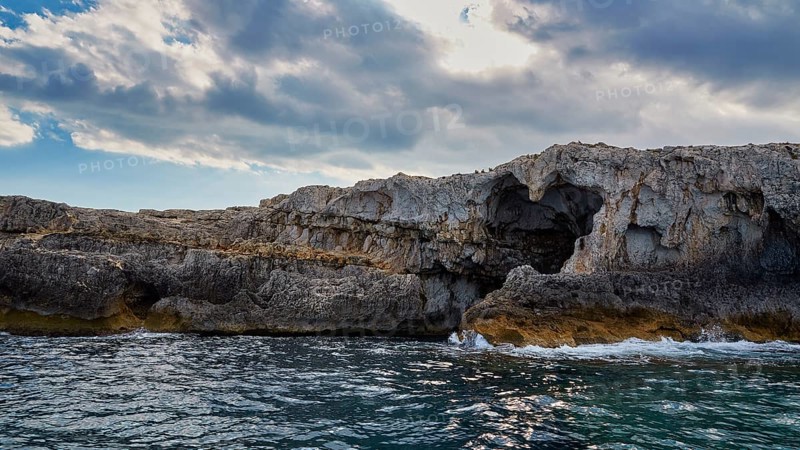 Dramatic rocky coastline with natural arch and cloudy sky over the sea, boat trip around the island of Ortigia, Isola di Ortigia, Syracuse, Sicily, Italy, Europe