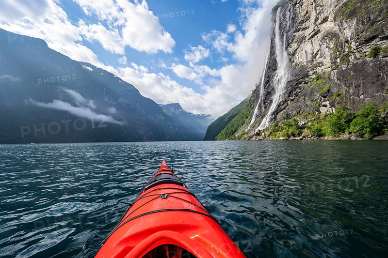 Kayak trip on the Geirangerfjord at the waterfall The Seven Sisters, tip of a red kayak in the fjord, atmospheric fjord landscape, first person view, near Geiranger, Møre og Romsdal, Norway, Europe