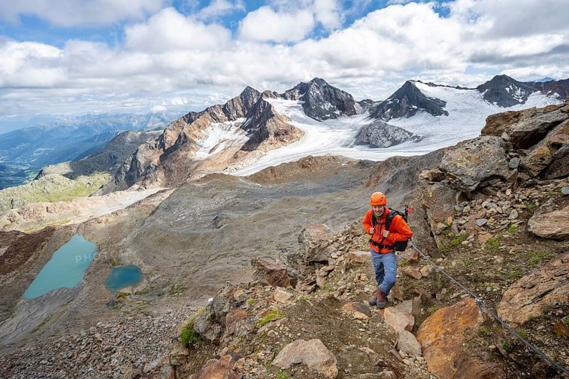 Mountaineer with helmet in high mountain landscape, view of blue glacier lakes, mountain peaks Königshofspitz and Hofmannspitze with glacier of the Übeltalferner, Stubai Alps, South Tyrol, Italy, Europe