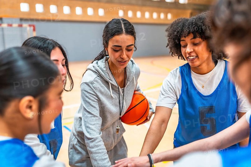 Female basketball coach motivating and inspiring her team during a time out, holding the ball and putting their hands together