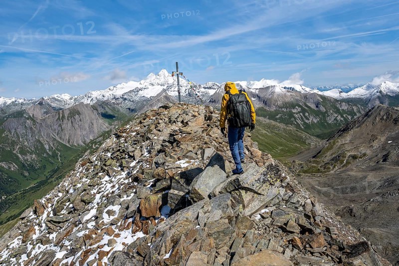 Mountaineers at the summit of Böses Weibl with summit cross and colourful prayer flags, view of picturesque mountain landscape with snow-covered summit of the Großglockner, Wiener Höhenweg, Schober group, Hohe Tauern National Park, Carinthia, Austria, Europe