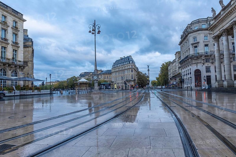 Comedie square in bordeaux city center with wet tram tracks reflecting surrounding buildings on a cloudy morning