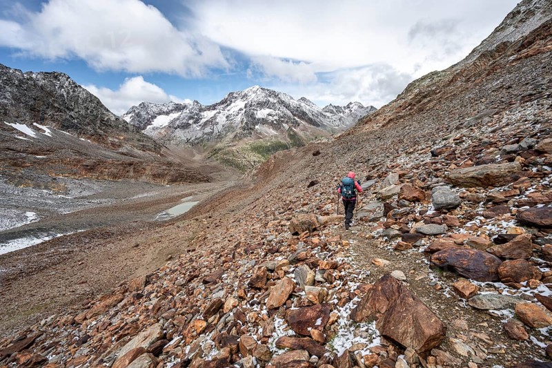 Mountaineer on hiking trail in steep rocky mountain landscape with fresh snow in summer, mountain peak Roter Knopf in the background, descent from the Hornscharte on the Wiener Höhenweg, Schober group, Hohe Tauern National Park, Carinthia, Austria, Europe