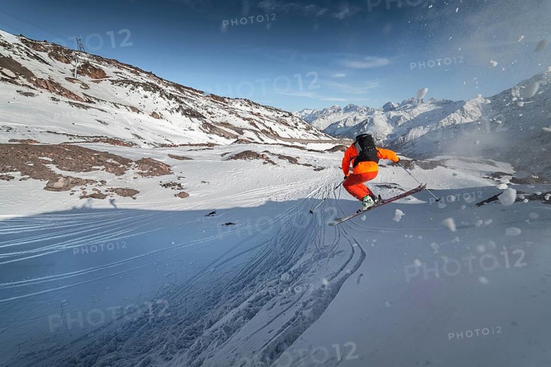 An athlete male skier jumps from a snow-covered slope against the backdrop of a mountain landscape of snow-covered mountains on a sunny day. The concept of winter sports
