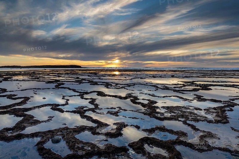 A beautiful sunset over the ocean with rocky beach and tidal pools in the foreground