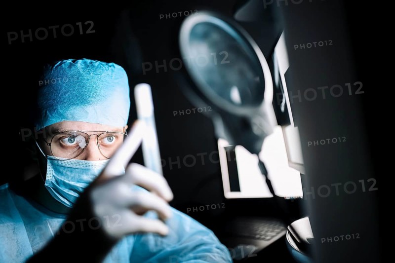 A surgeon in an operating room intently examining a test tube under a magnifying glass