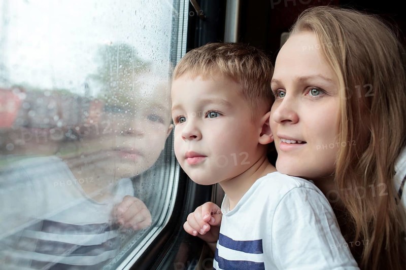 Mother and son looking through a train window as they enjoy a days travel with the small boys face reflected in the glass