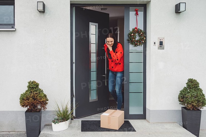 Cheerful young woman excited over a package she just received. Woman getting her christmas gift in the mail. Opening the Christmas present at home