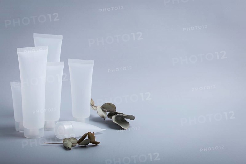 White empty plastic cosmetic tubes staying at gray background with eucalyptus branches, concept of cosmetology, body and skincare, beauty industry, food photography, food photography