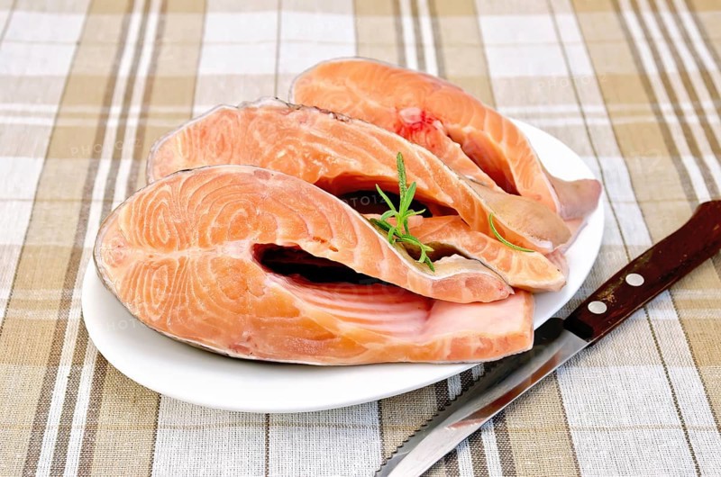 Three pieces of trout in white plate with rosemary on a checkered cloth background