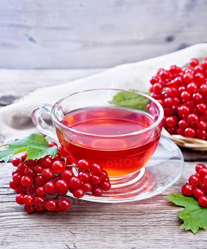 Tea with viburnum in a glass cup, wicker plate with berries, green leaves and burlap on wooden board background
