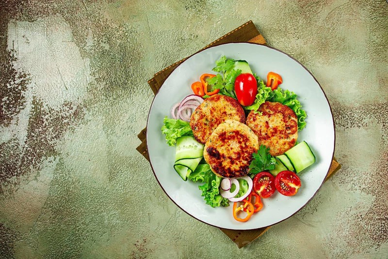 Fried chicken cutlets, minced chicken, with vegetables, on a green background, with vegetable salad, top view, homemade, no people