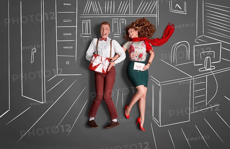 Happy valentines love story concept of an office romance. Young couple at work smiling at each other and exchanging gifts against chalk drawings office background