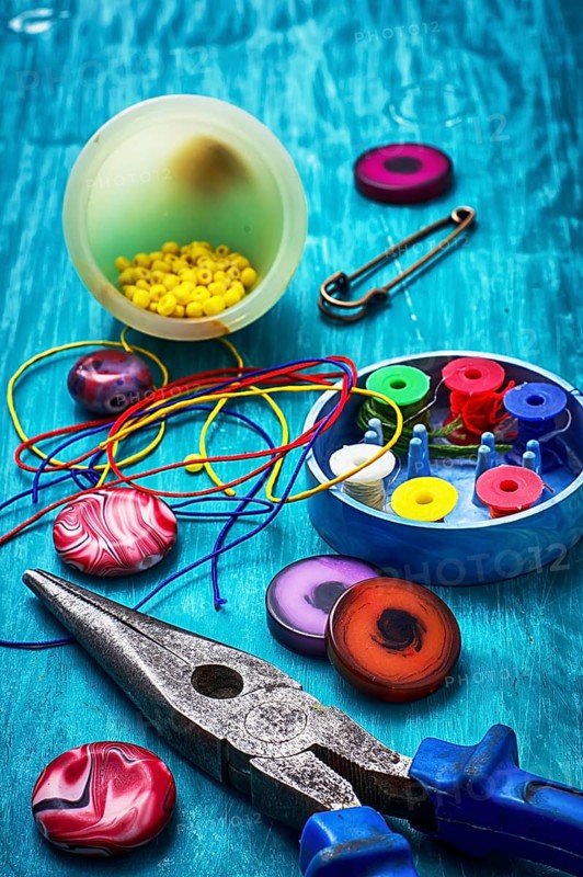 Beads, pliers and other needlework accessories on outdated turquoise wooden background