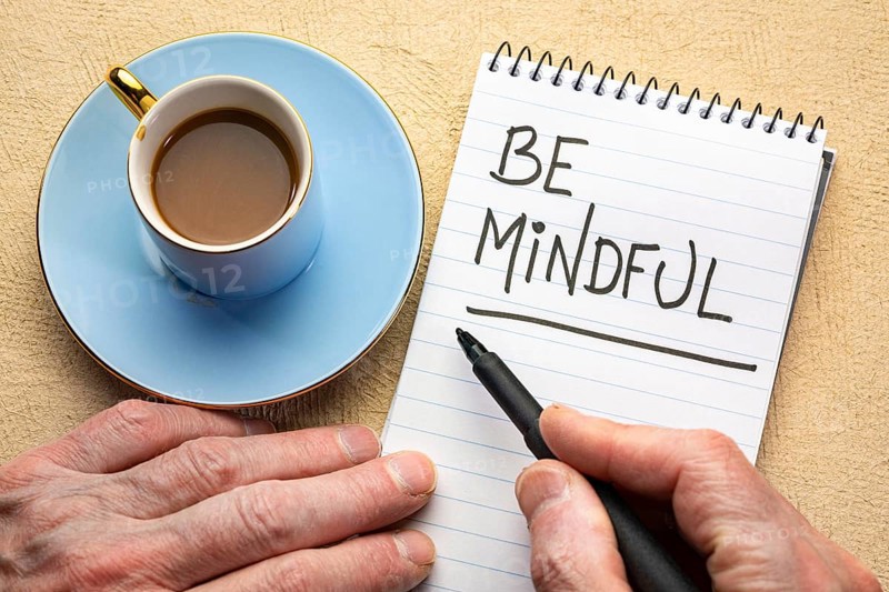 Be mindful - man hand writing a note with a black marker in a spiral notebook