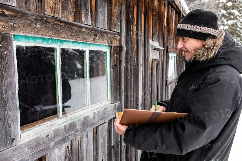 Middle aged home Inspector taking notes on a notebook with leather cover during an outdoor inspection. examining a window of old wooden house