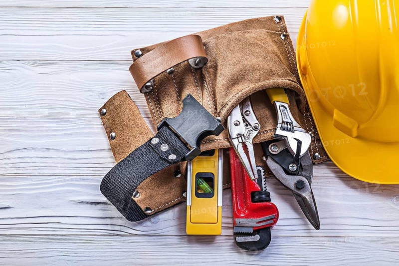 Collection of construction tooling in leather tool belt safety building helmet on wooden board