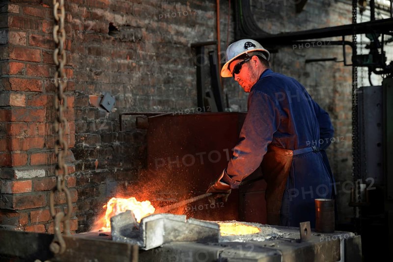 A foundryman clears slag from the molten iron in the furnace