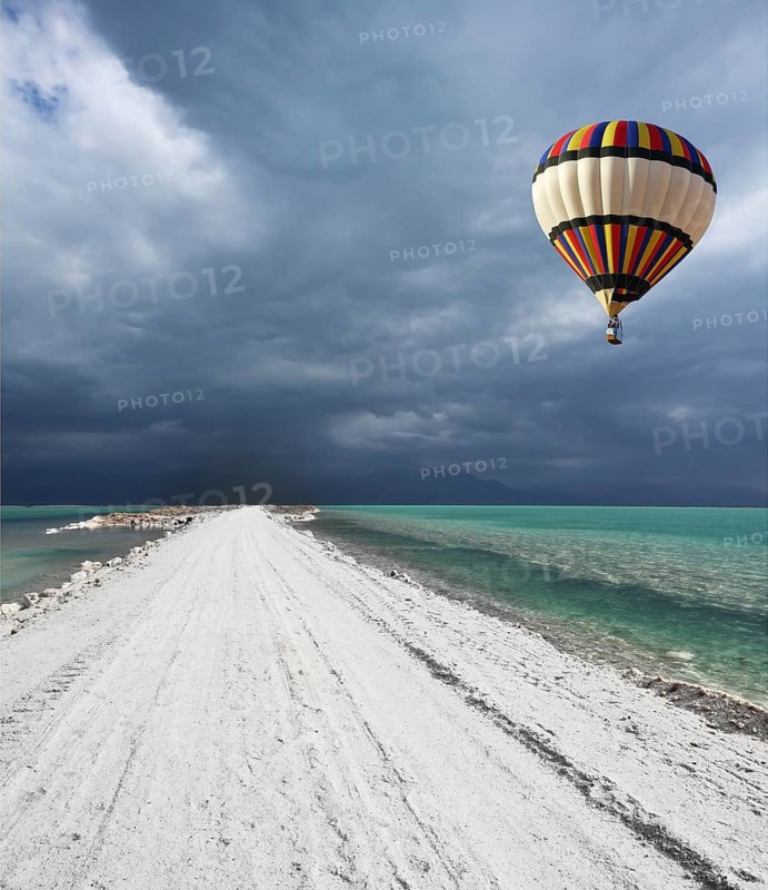 Picturesque bright balloon with a basket of passenger flying in a thunderstorm over the Dead Sea