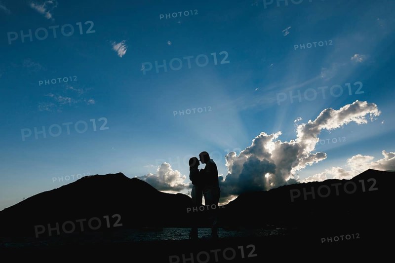 Silhouettes of a man and a woman who hug and kiss at sunset on the seashore against the background of mountains .