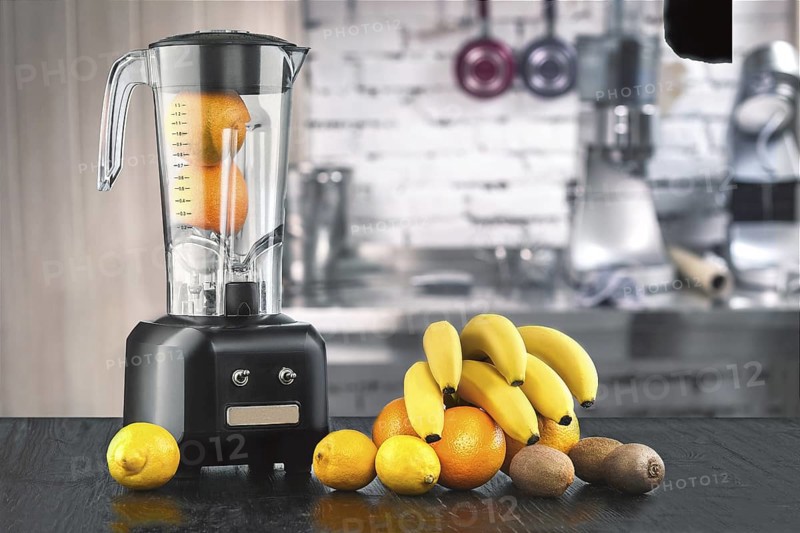Metal food blender close-up with fresh exotic tropic fruits next to it on kitchen background with empty space. Blender and wooden table in kitchen