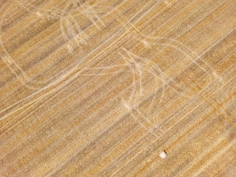 Striking tracks and patterns from a tractor on a dry agricultural field with straw bales, aerial view from Germany
