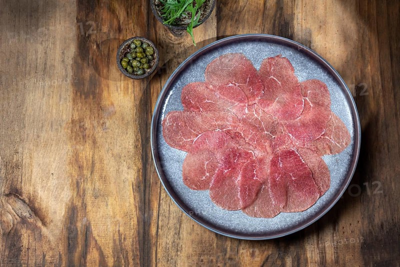 Food, Marbled beef for carpaccio with ingredients arugula and capers on gray plate, wooden background, top view