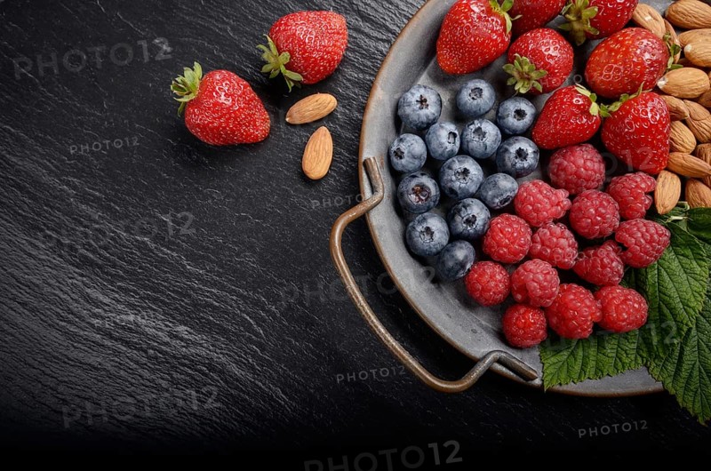 Tray with ripe organic bilberry raspberry strawberry and almonds set on slate closeup