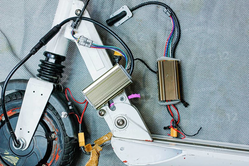 Electric scooter with exposed components and wiring, showcasing mechanical details on a grey surface