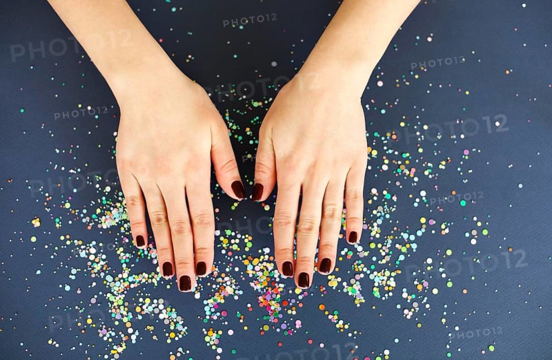 Top view of crop anonymous female with bright manicure over dark blurred background with colorful confetti